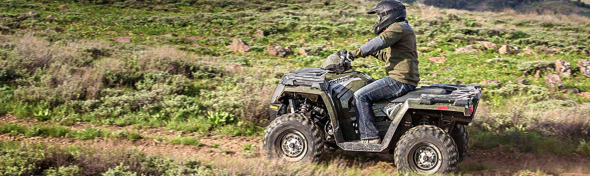 Man riding a Polaris® Sportsman 450 through a grassy field.