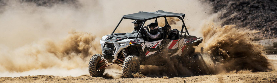 Three occupants taking a sharp turn in a field of dust within a Polaris® RZR XP 4 1000.